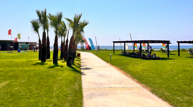 Grünanlage im ROBINSON Cyprus mit Palmen, Liegebereichen, Wassersportstation und Meerblick