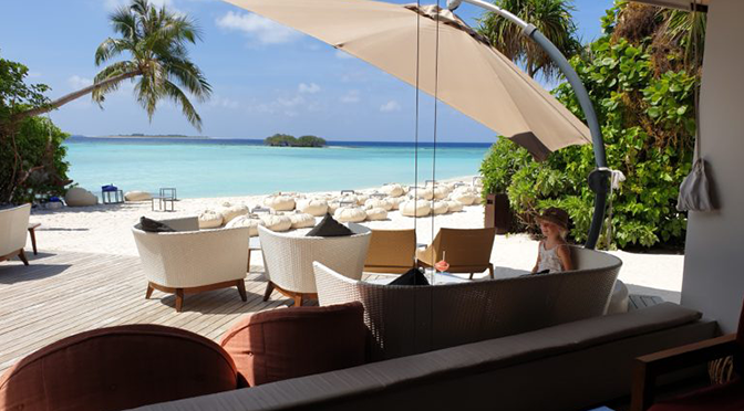 Lounge-Bereich im ROBINSON Noonu mit Blick auf türkisblaues Meer und weißen Sandstrand