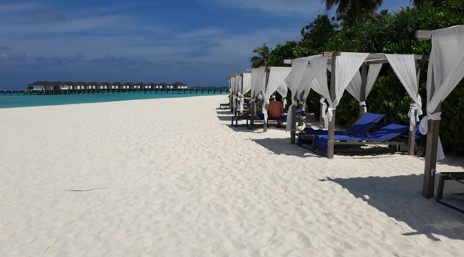 Weiße Daybeds am Strand des ROBINSON Noonu mit Blick auf Overwater-Villen